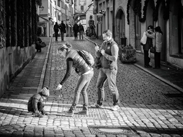 As we can see in the image there are buildings, clock, few people and dustbin. The woman standing...