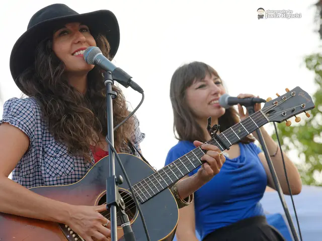 There are 2 women standing and playing guitar and singing on the microphone.