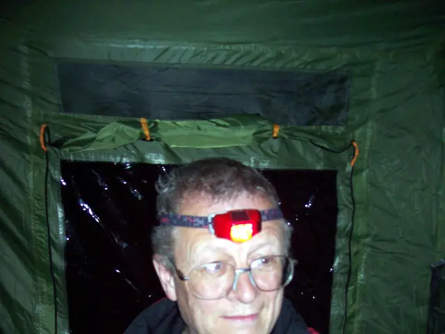 In the image there is an old man in red jacket is in the front, inside a tent, he is having a torch...