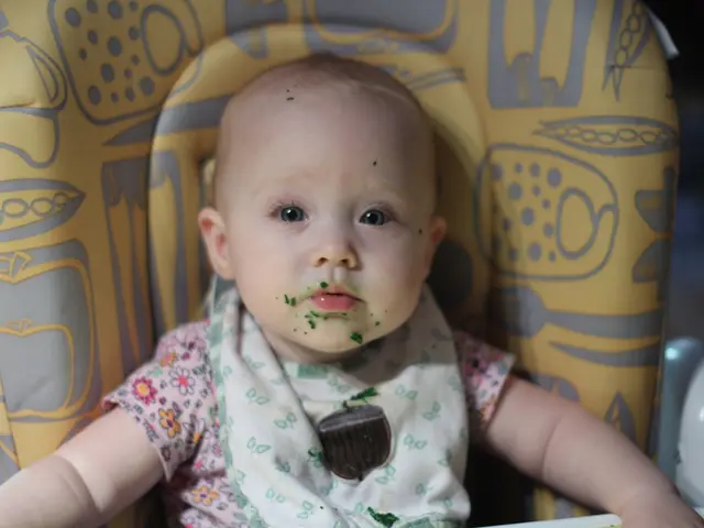 In this picture there is a kid sitting on a chair. In the background of the image it is blurry.