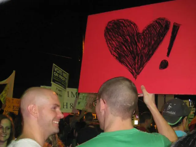 In this picture there are two men standing and holding the red color heart board. Behind there are...