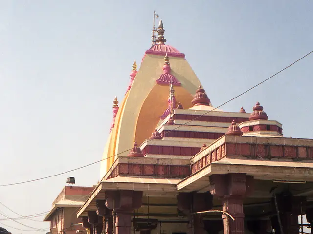 In the picture we can see a temple with a pillar in it and near to it, we can see many devotees and...